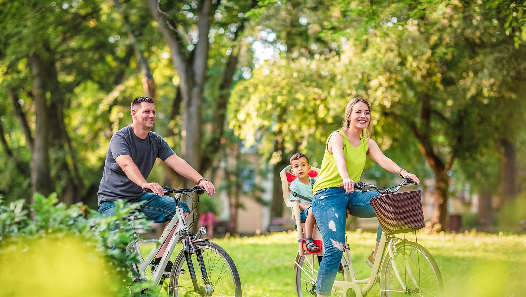 mom and dad riding bikes in a park with a young child on the back of one of the bikes